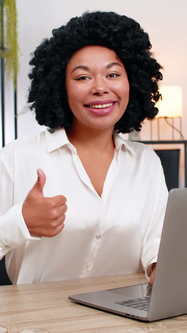 Donna d'affari afroamericana fa il pollice in su davanti al laptop, sorridendo per un risultato di successo oggi.