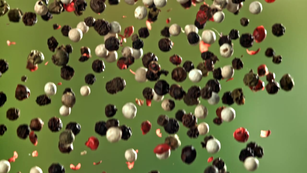 Mixed Peppercorns Falling in Slow Motion Against Green Background