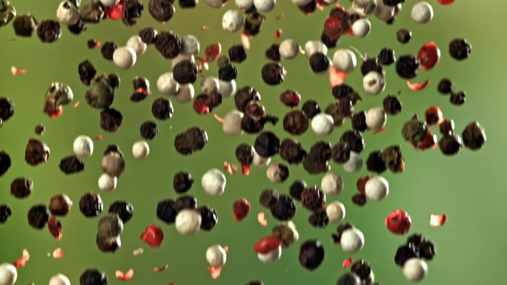 Mixed Peppercorns Falling in Slow Motion Against Green Background