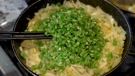 adding chopped green beans to saucepan on top of sliced potatoes and onions