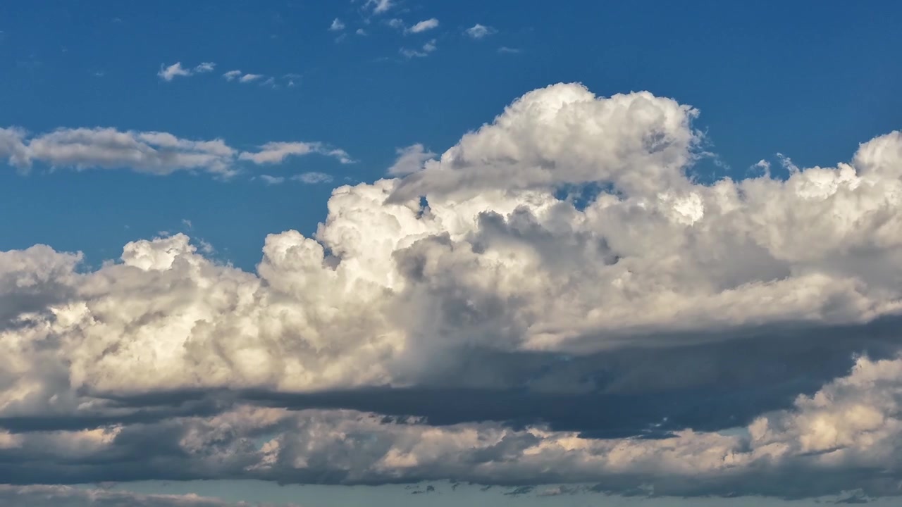 4K drone timelapse of a picturesque cloudscape reminiscent of classic Southwestern paintings. Bright, fluffy cumulus clouds drift across a vibrant blue sky above a high desert landscape.