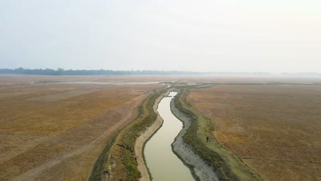 Aerial-drone-shot-capturing-windy-river-flowing-through-plains-and-countryside