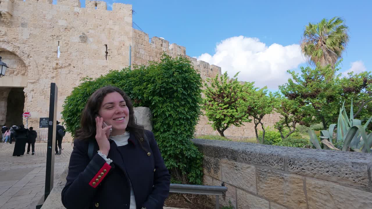 Young adult woman talking on phone near Jerusalem old city walls, Zion Gate. Slow motion.