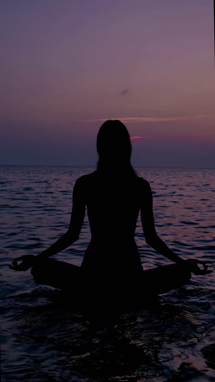 Silhouette of a person meditating by the sea at sunset, captured from a low angle