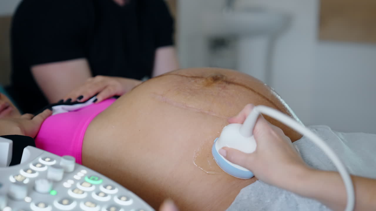Cropped image of a pregnant lady on ultrasound check up. Doctor moves the device by the big abdomen.