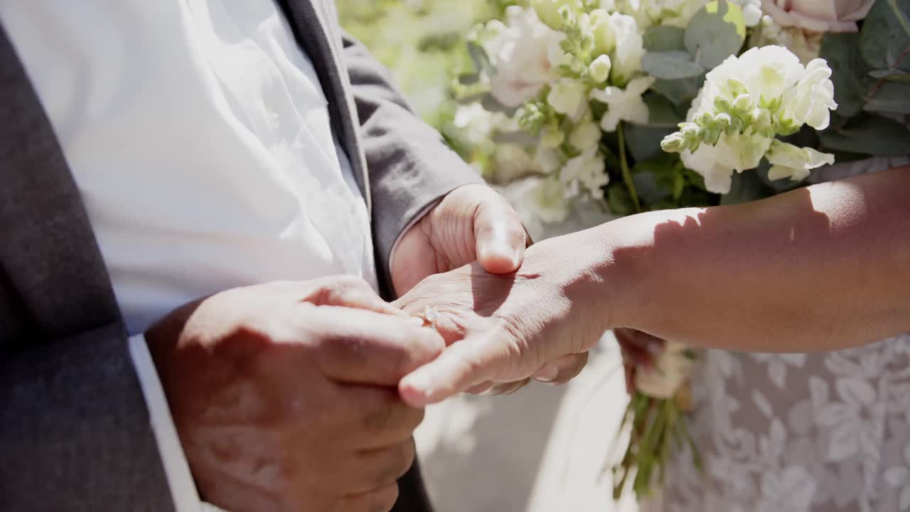 정원 에서 결혼식 을 하는 동안 결혼 반지 를 교환 하는 노인 두 인종 부부 의 중간 섹션, 느린 동작