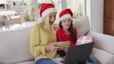 Mother-and-daughter-holding-gift-boxes-while-having-a-video-chat-on-laptop-at-home