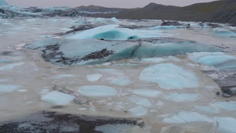 Static,-shot-of-small,-turquoise-icebergs,-at-skaftafellsjokull-glacier,-snowy-mountains-in-the-background,-on-a-cloudy-day,-in-South-coast-of-Iceland