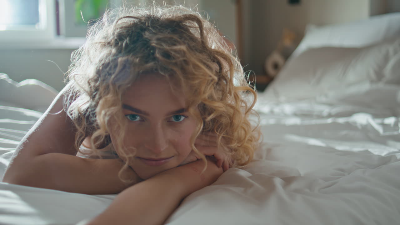 Ragazza spensierata che si stira a letto al sole del mattino. Donna calma e sensuale che guarda in camera.