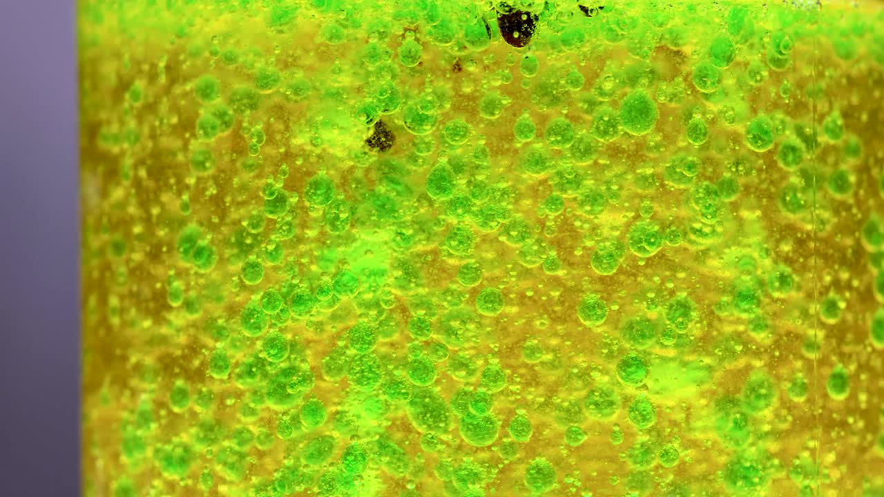 ярко-зеленая и желтая химическая реакция в чашке, демонстрирующая динамическое движение пузыря и разделение плотности