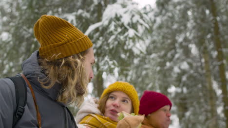 vista inferior de tres amigos sentados y hablando mientras comen en un bosque nevado