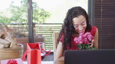 feliz mujer biracial con vitiligo haciendo una videollamada del día de san valentín en una computadora portátil, oliendo rosas