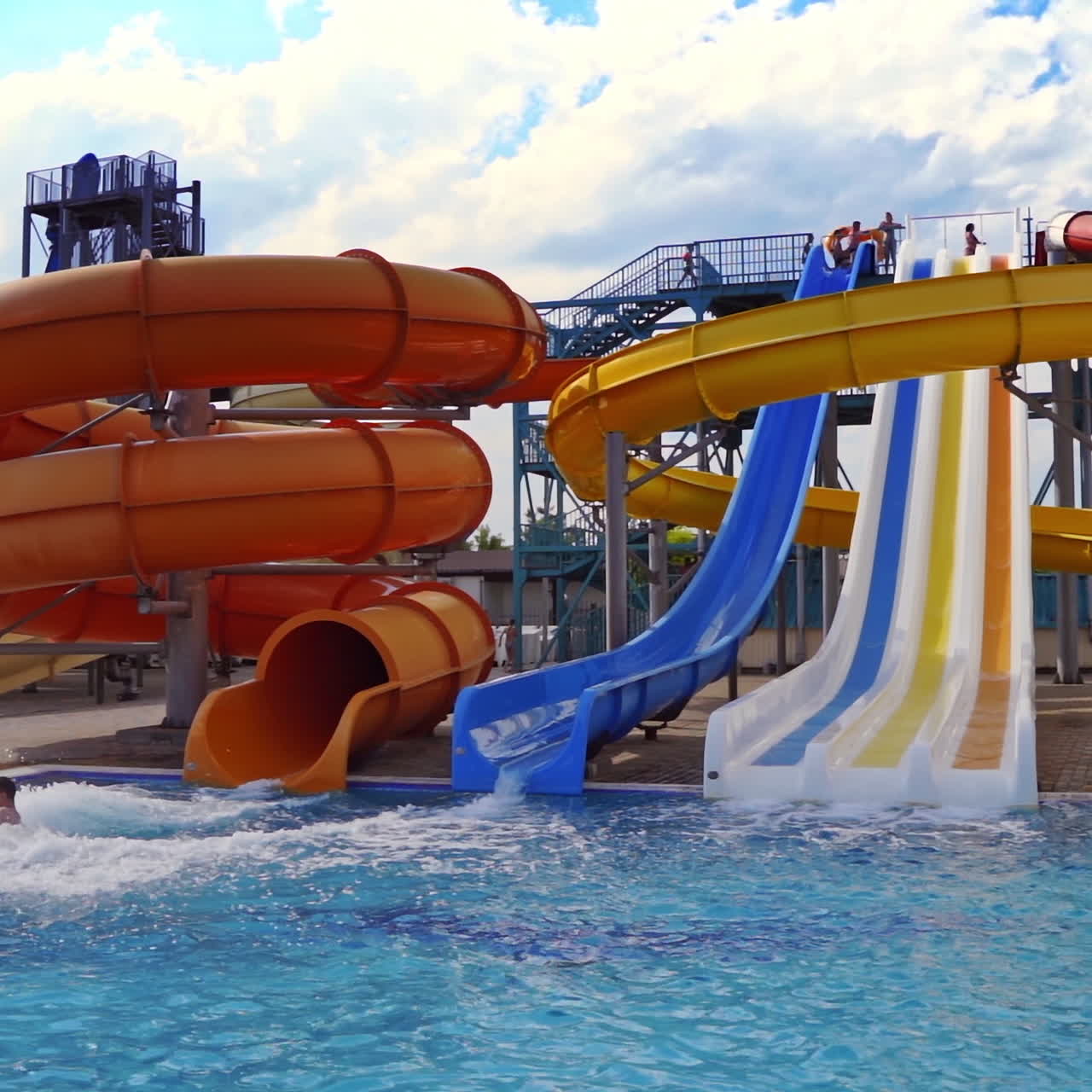 Beautiful aquapark under blue sky. Colorful slides with clear water in the swimming pool outdoors. Joyful entertainment in the open air in a summertime.