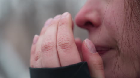 close-up face view of young woman rubbing her nose with black long sleeve in cold weather, her flushed skin highlights the winter chill. blurred background of trees