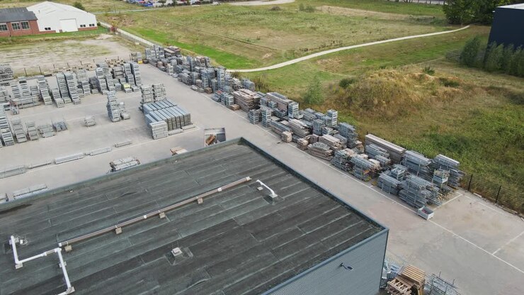 Drone flying over a warehouse on an industrial storage yard with neatly organized stacks of construction materials