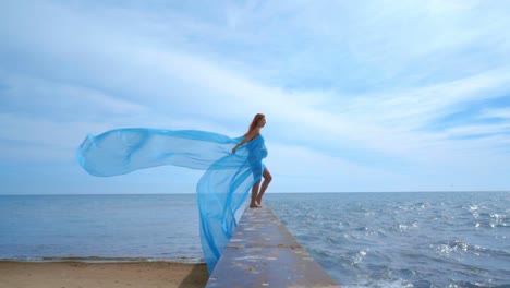 pregnant woman with fabric flying wind on sea beach. young woman