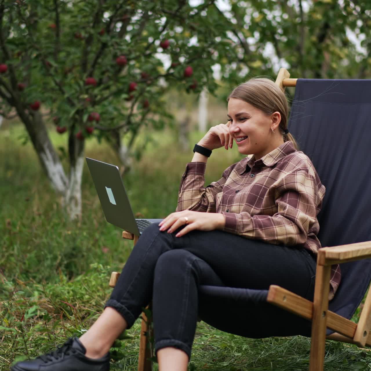 Donna caucasica che guarda un video sul laptop seduta all'aperto. La donna sorride felicemente e poi sembra stupita. Natura sullo sfondo