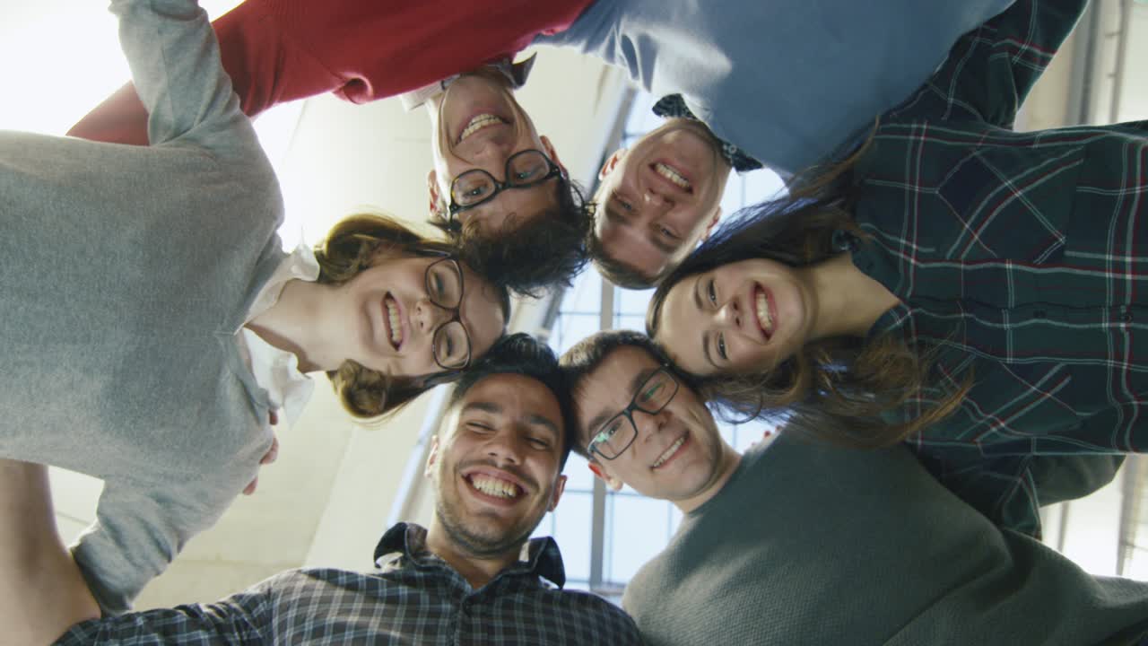Multi-ethnic group of happy young students are standing in a circle and looking down at the camera.