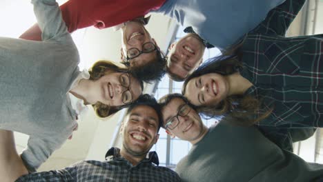 multi-ethnic group of happy young students are standing in a circle and looking down at the camera.