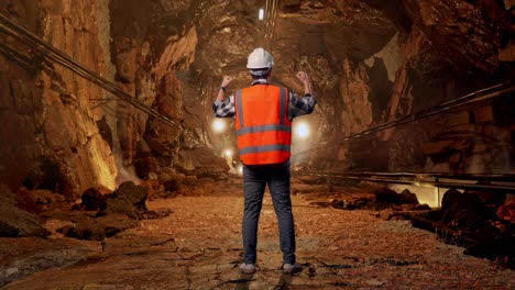 full body back view of a male engineer with safety helmet raising his hands celebrating while working in underground mine tunnel