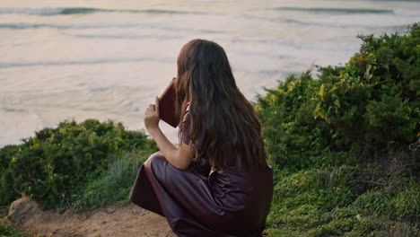 relaxed woman holding book sitting in front ocean closeup. girl enjoy reading.