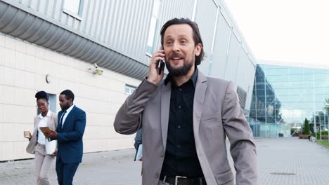 caucasian businessman in stylish clothes walking down the street and talking on the smartphone