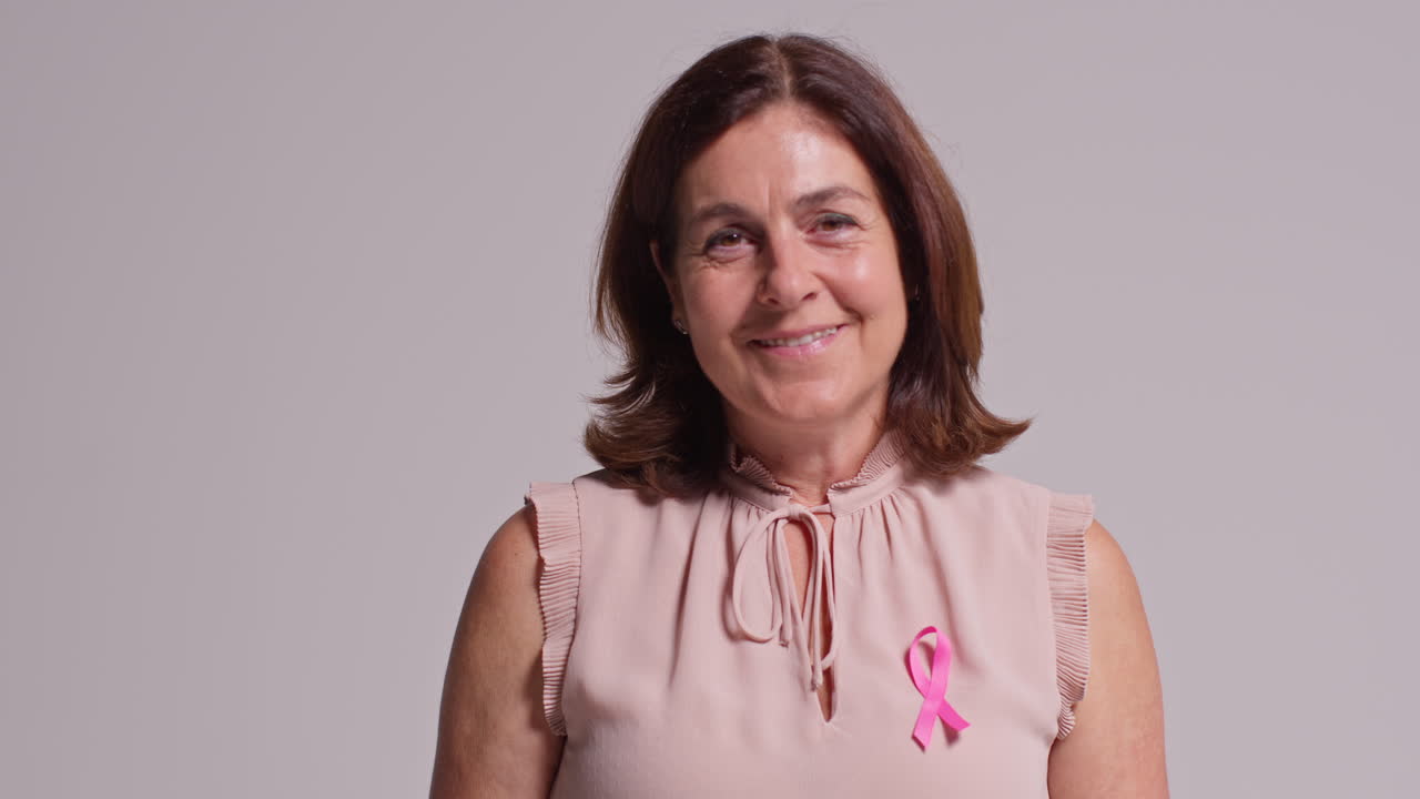 retrato de estudio de una mujer madura sonriente que lleva una cinta rosa de concienciación sobre el cáncer de mama contra un fondo blanco 1