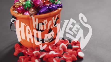 Animation-of-happy-halloween-text-over-pumpkin-bucket-and-sweets