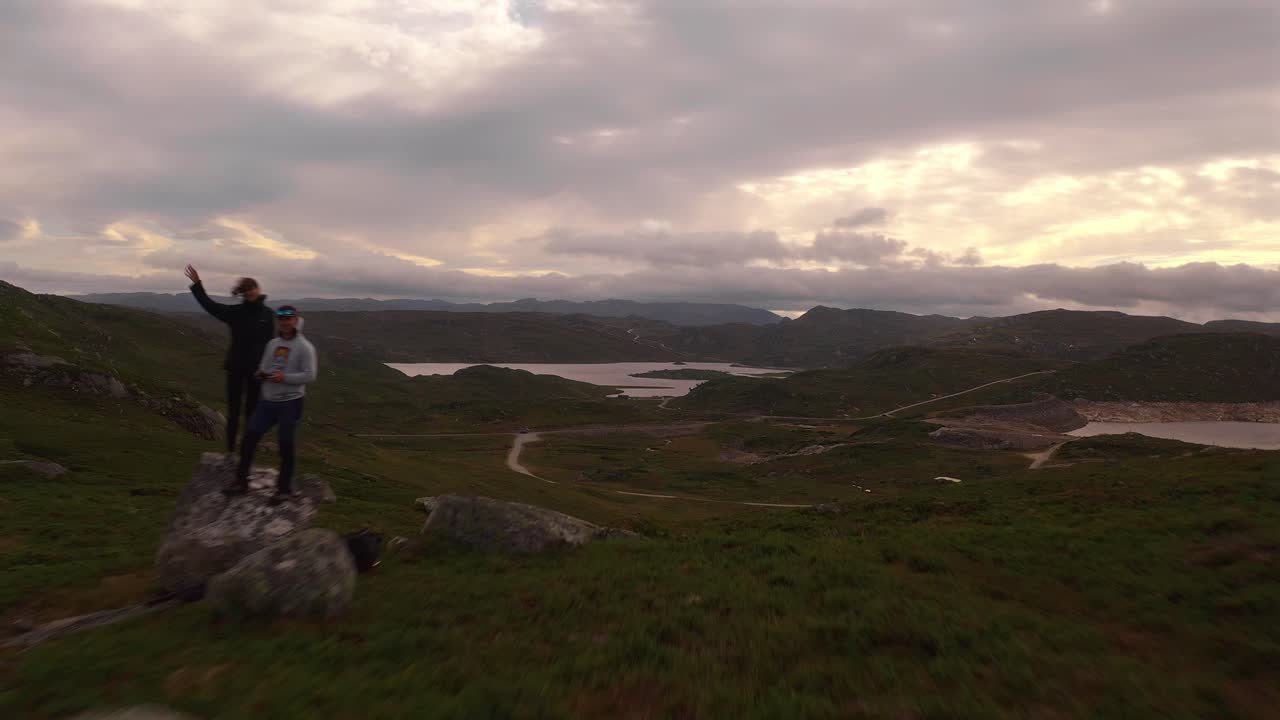 View of scenic Norwegian landscape with winding road and two people on a cliff