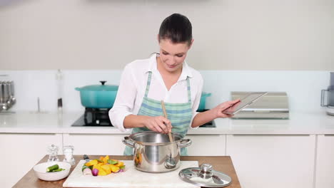 hermosa morena siguiendo una receta en su tableta mientras hace la cena