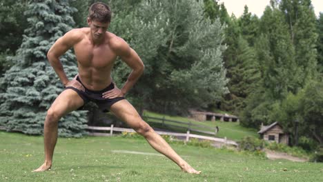 4k young caucasian fit attractive male exersicing outdoors with green vegetation background adductor mobility exercise