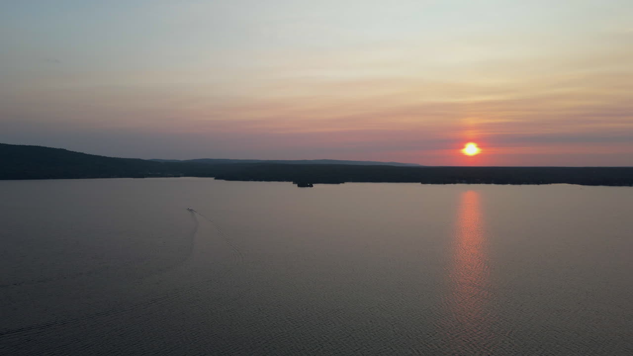 Aerial shot of boat driving towards beautiful sunset over lake and forest covered hillside. Calagbogie Ontatio