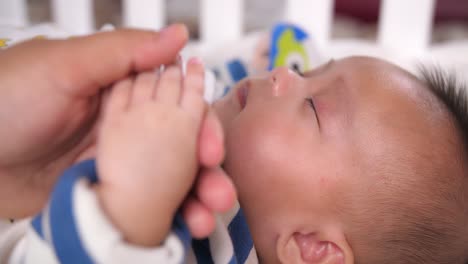 baby sleeping with hand held by parent