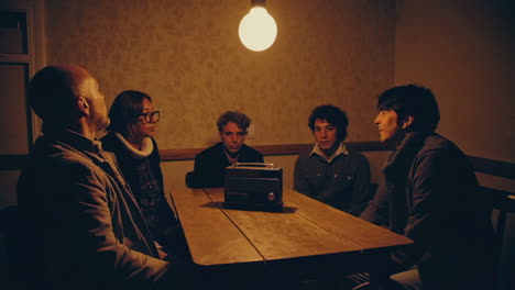 people sitting around a table, listening to a radio