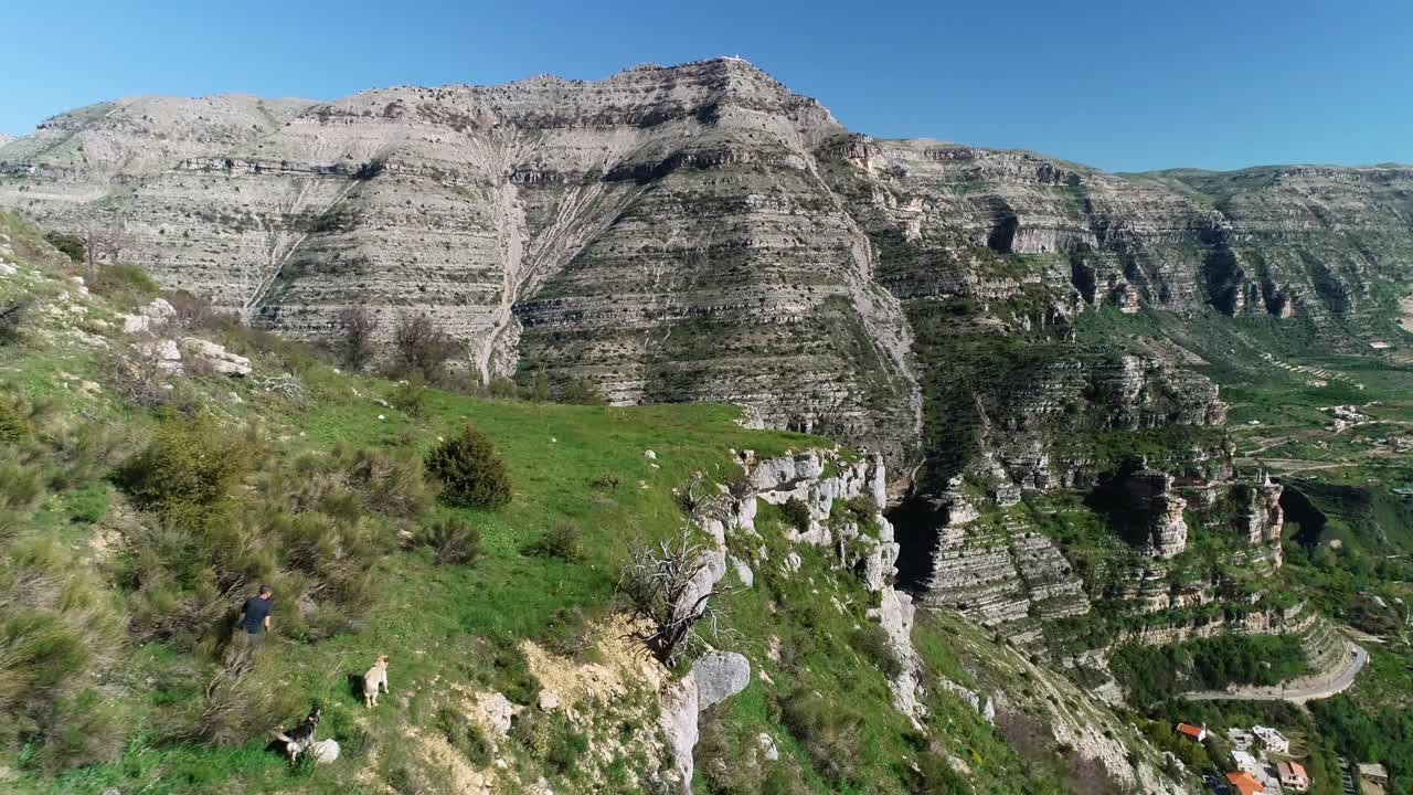 산 가장자리에 위험하게 가까운 두 마리의 개와 함께 달리는 백인 남자, 공중 접근