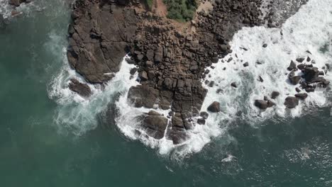 Looking-straight-down-as-ocean-waves-crash-in-white-onto-coastal-rocks