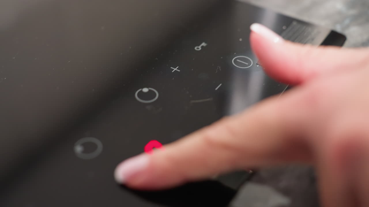 Closeup of baker hand switching on electric cooker by pressing power button followed by minus button to reduce heat, demonstrating precise control, modern kitchen use, and smart cooking technology