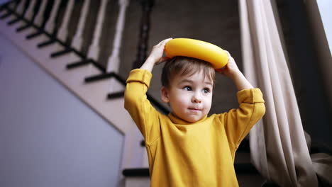 smiling dark-haired baby boy putting the pyramid ring on his head. kid drops the toy and smiles adorably. low angle view.
