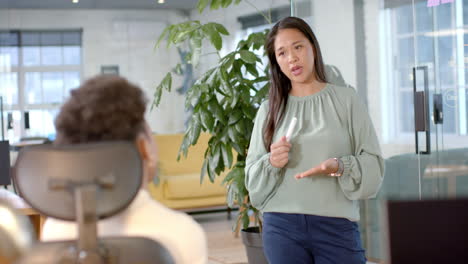 asian businesswoman standing, talking to african american colleague seated