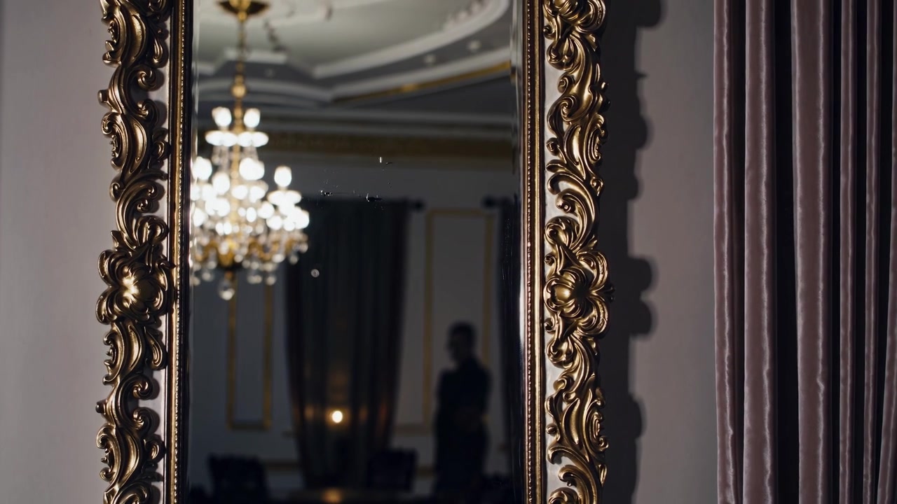 Verzierter goldener Spiegel, der einen Kronleuchter und eine Silhouette in einem eleganten Zimmer widerspiegelt