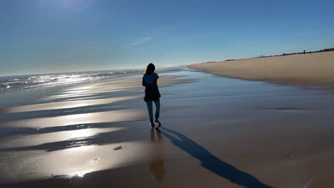 young woman walking on a desert beach under sunset light