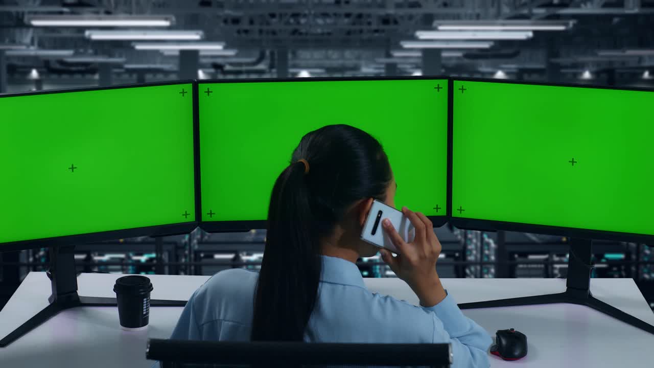 데이터 센터에서 여러 컴퓨터 모니터를 모의로 작업하는 동안 휴대 전화로 대화하는 아시아 여성의 뒷면