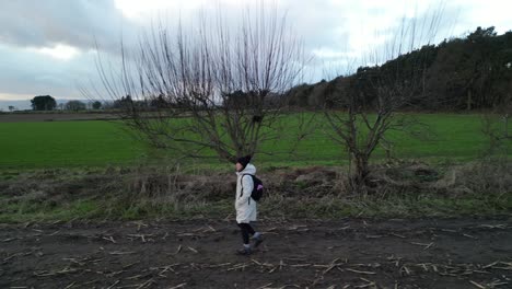 woman walking resolutely across trail through winter fields, aerial drone parallel pan, cheshire, uk