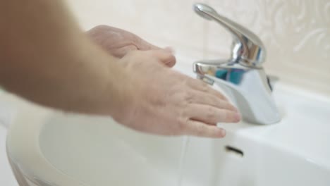 man washes hands in bathroom sink