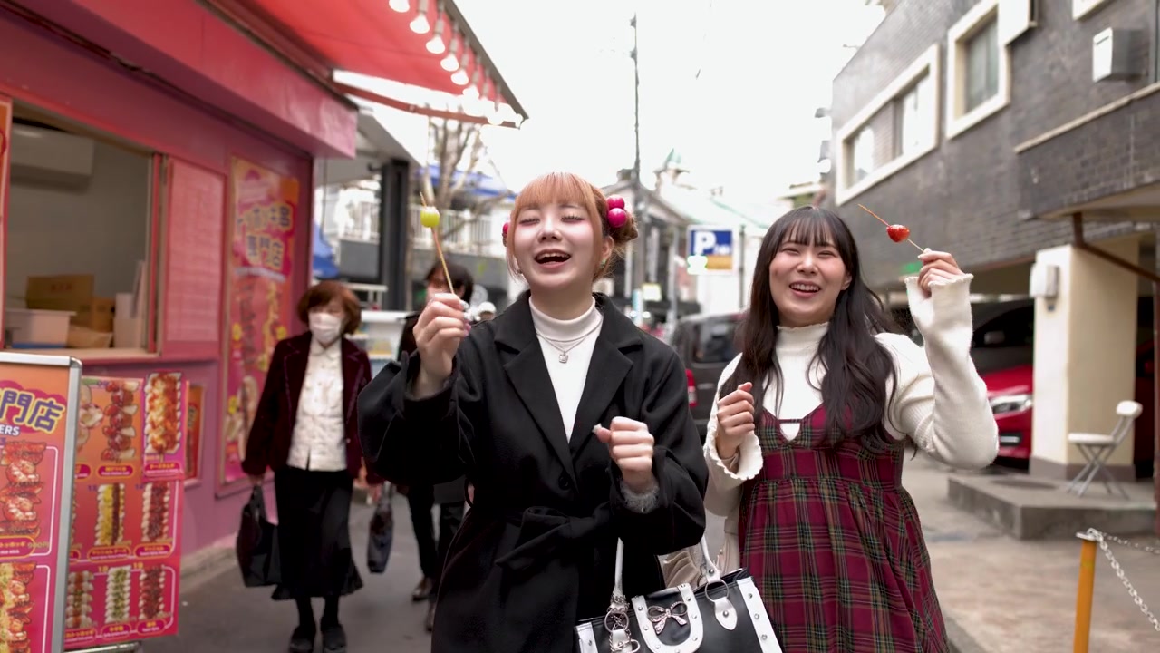 Amici asiatici allegri che tengono spiedini di frutta candita mentre camminano per la strada di Harajuku a Tokyo, Giappone