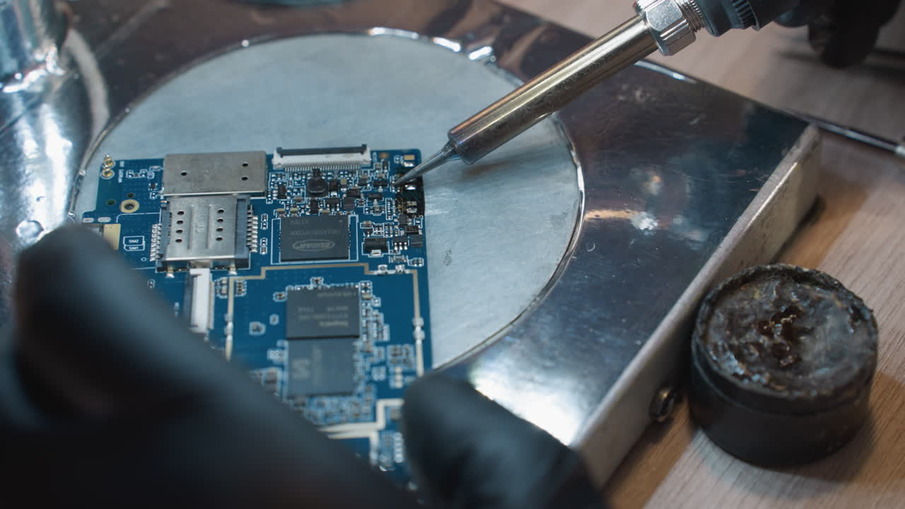 una vista de cerca de un soldador y una placa de circuitos impresos (pcb) en una superficie metálica, con alguien trabajando en el circuito con soldador