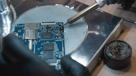 a close-up view of a soldering iron and a printed circuit board pcb on a metallic surface, with someone working on the circuit with soldering iron