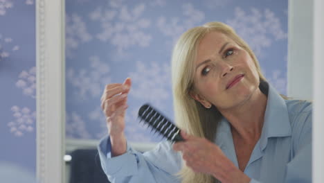 mujer madura en la menopausia que sufre pérdida de cabello cepillándose el cabello en el espejo en casa