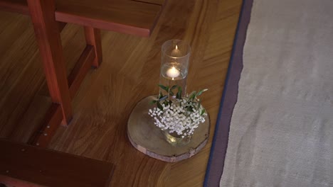 single candle in a glass holder with a small bouquet, placed on a wooden base along a church aisle