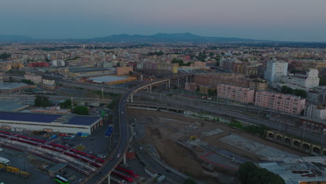 Aerial-descending-footage-of-transport-infrastructure-in-city.-Cars-driving-on-road-bridge-over-modern-high-speed-train-units-parking-on-track.-Rome,-Italy